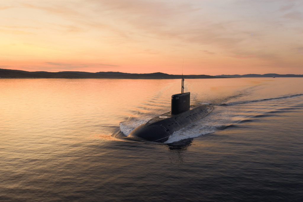 A submarine moves through the water at sunset.